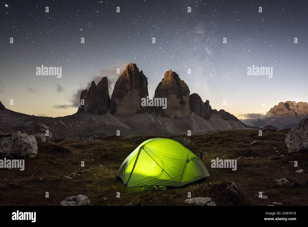 Green tent lighted from the inside against the backdrop of incredible starry sky and Three Peaks of Lavaredo mountains. National Park Tre Cime di Lavaredo, Dolomites, Italy. Landscape photography Stock Photo