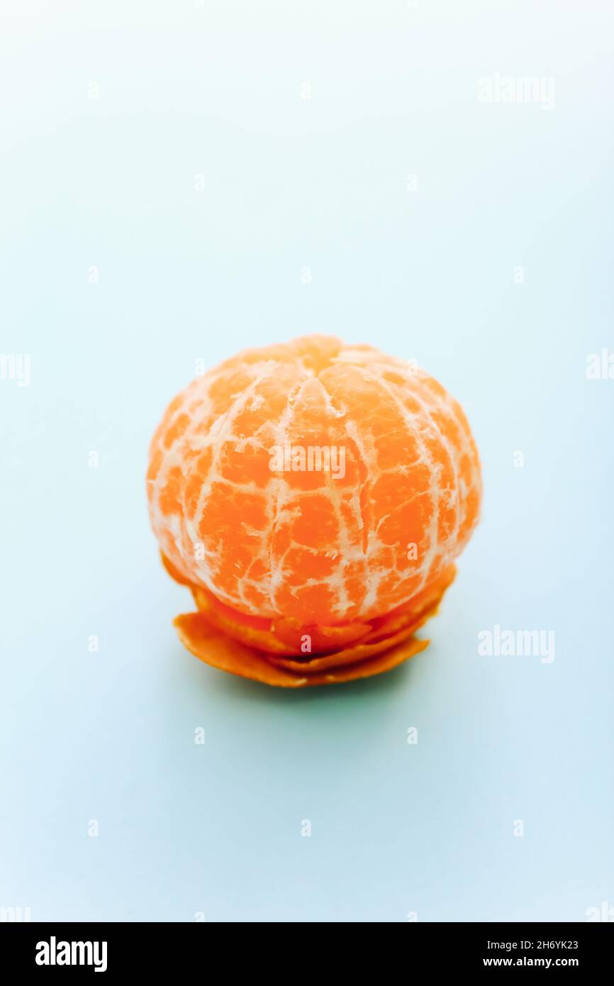 One peeled tangerine on light blue background Stock Photo
