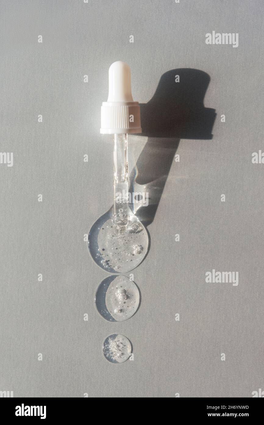 Drops of hyaluronic acid and pipette on light gray background with hard shadows. Top view, flat lay. Stock Photo