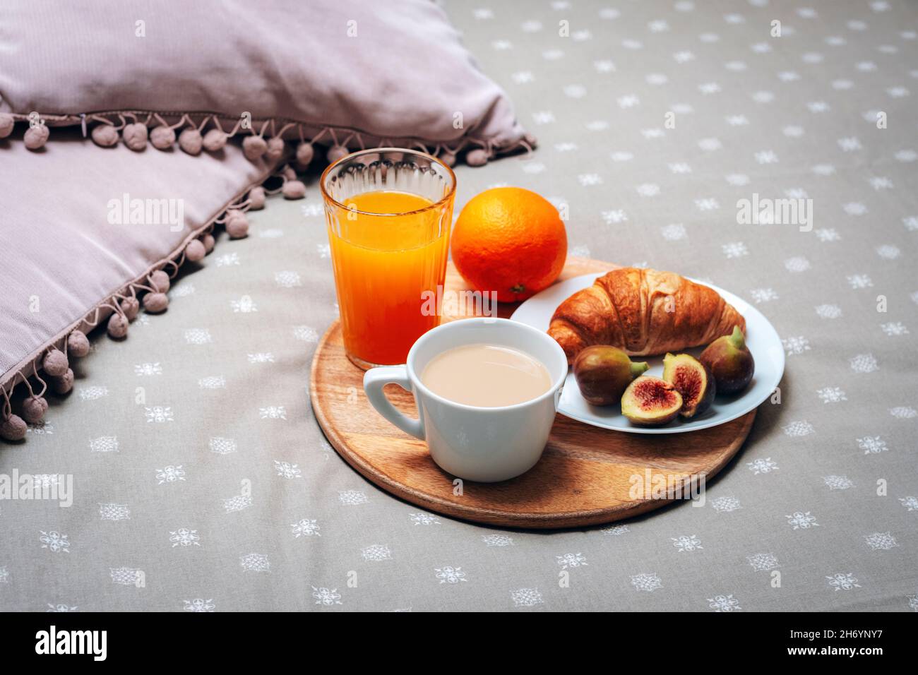 Breakfast in bed. Croissant and figs on a plate, a coffee cup, orange juice and an orange on a tray. Close up. Stock Photo