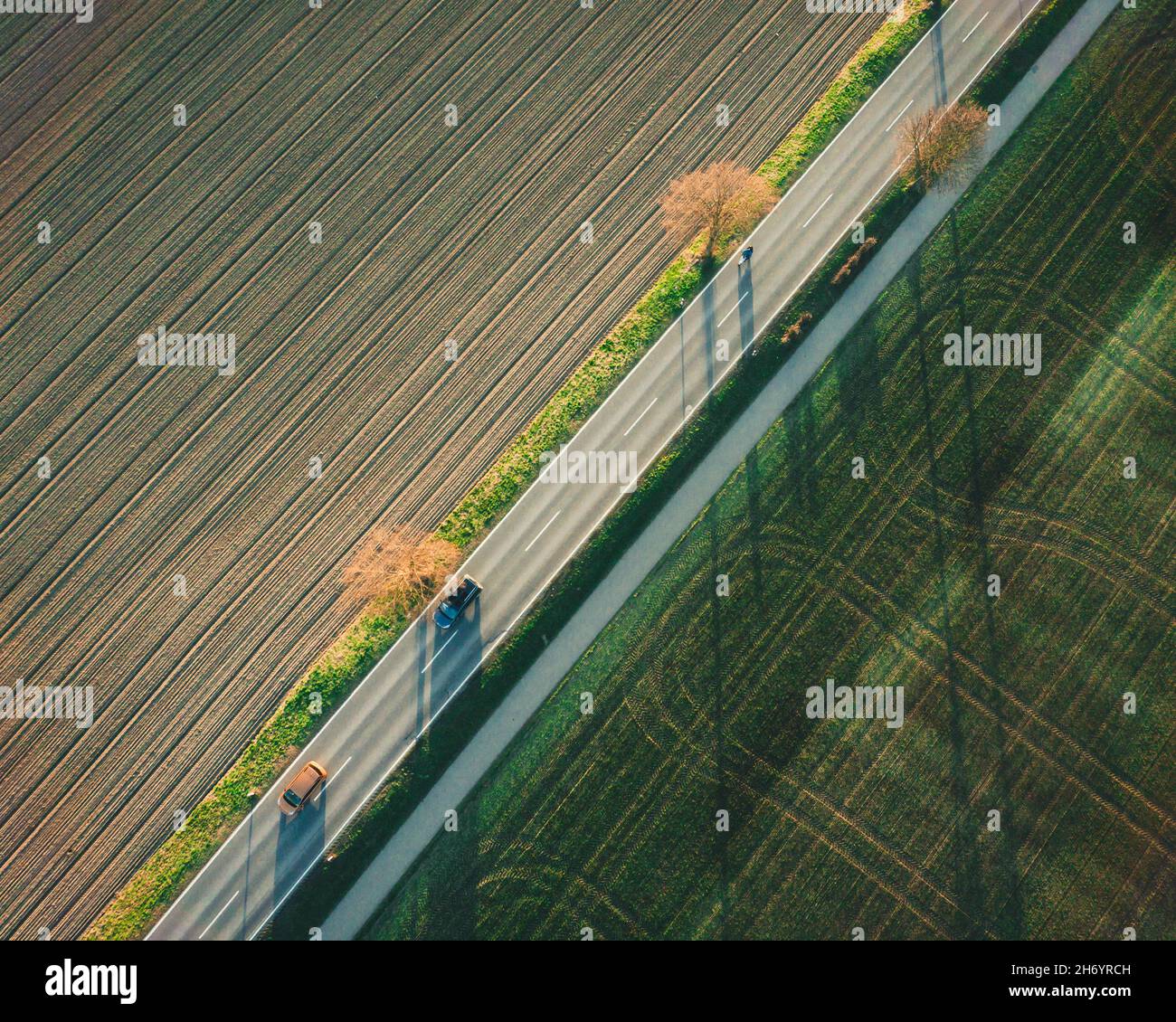 Aerial shot of a thin road going through a beautiful green grass field ...