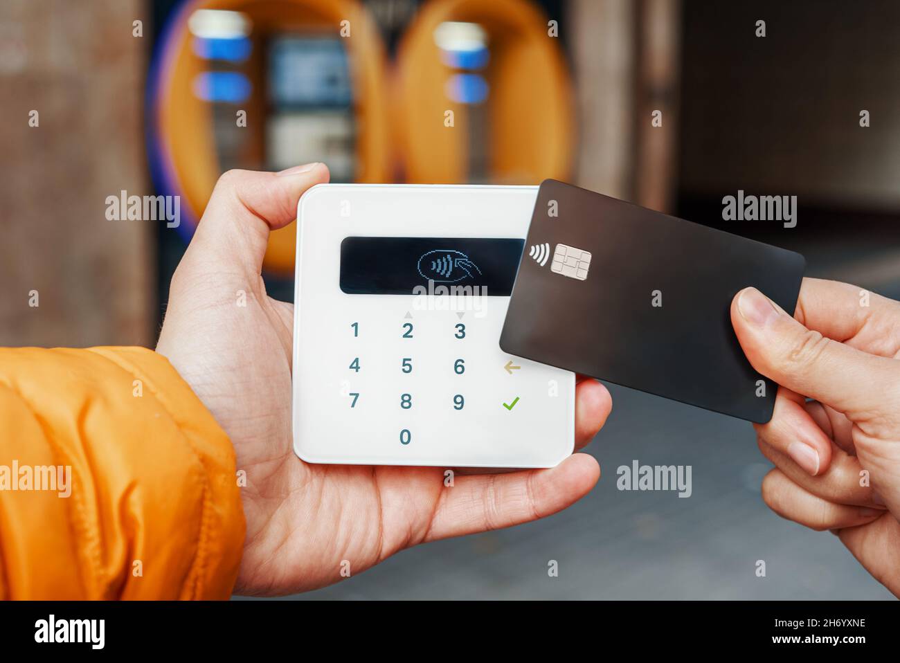 Unrecognizable customer with contactless black credit card paying to seller with terminal on blurred background of bank ATM. Concept of termination of cash Stock Photo