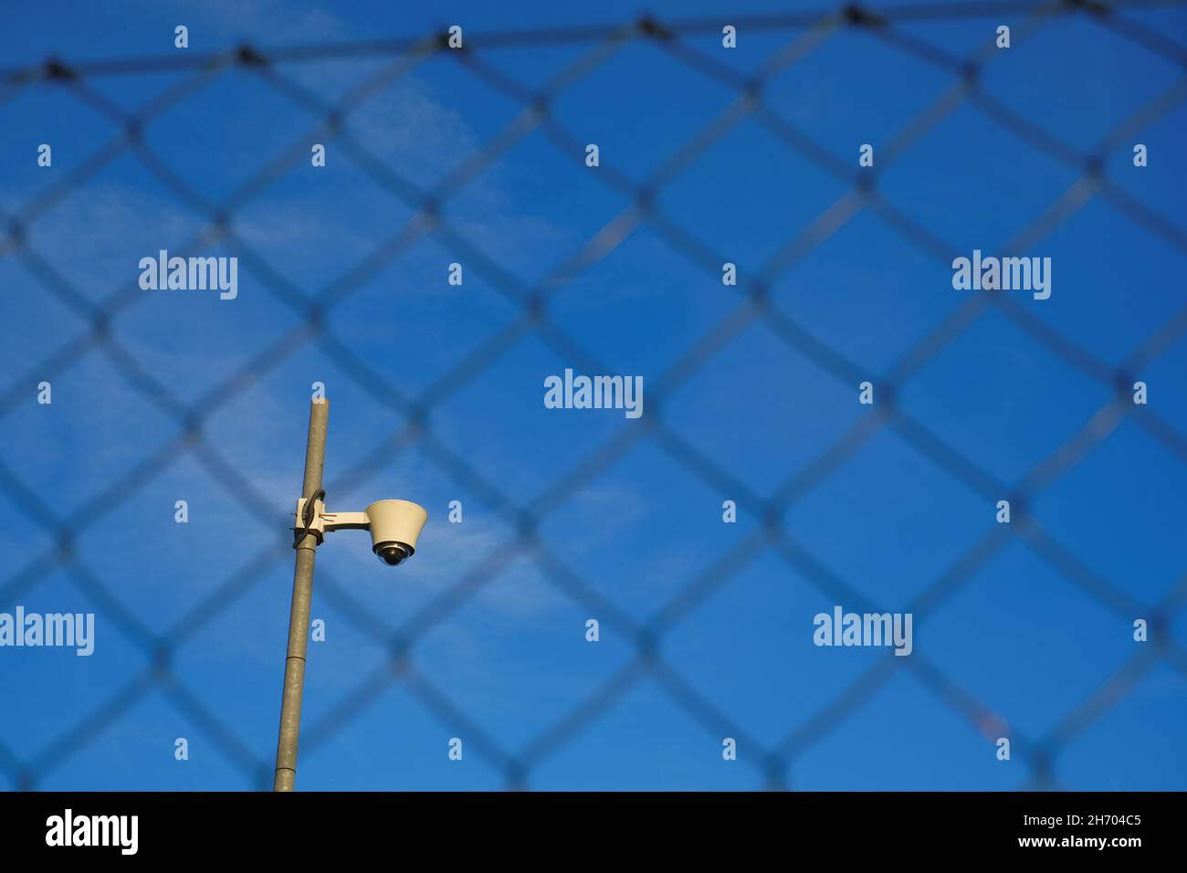 Surveillance Camera.Video surveillance . Camera behind metal grid on bright blue sky background. Closed area. Stock Photo