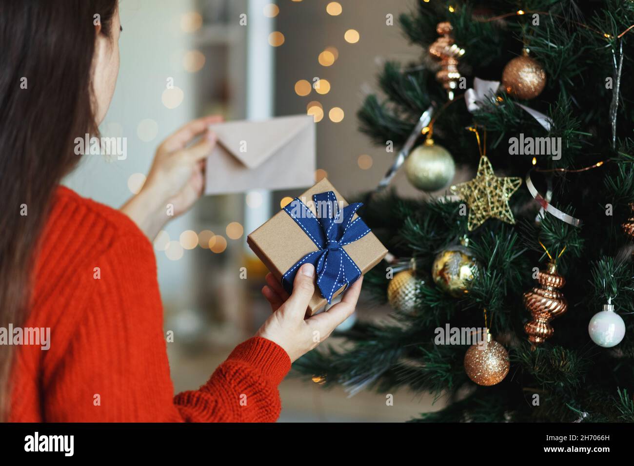 Woman prepare xmas gift box with greeting card or letter for family, christmas tree background. Stock Photo