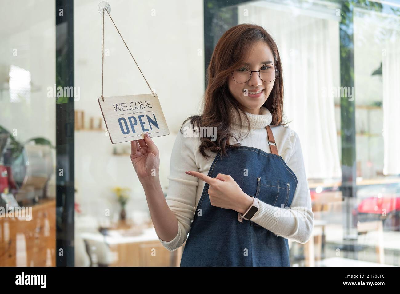 Portrait asian woman smiling and looking to camera in coffee shop. Barista female holding open sign in hand. Working woman small business owner or sme Stock Photo