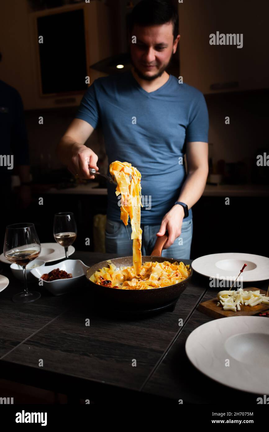 Man sets the table, homemade pasta, bacon, feta and tomatoes, cheeses