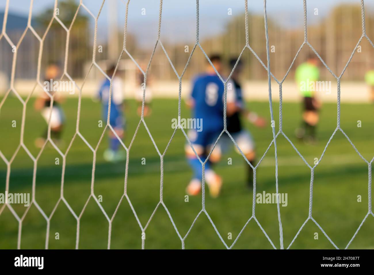 Football game in arena through soccer nets. Blurred players background