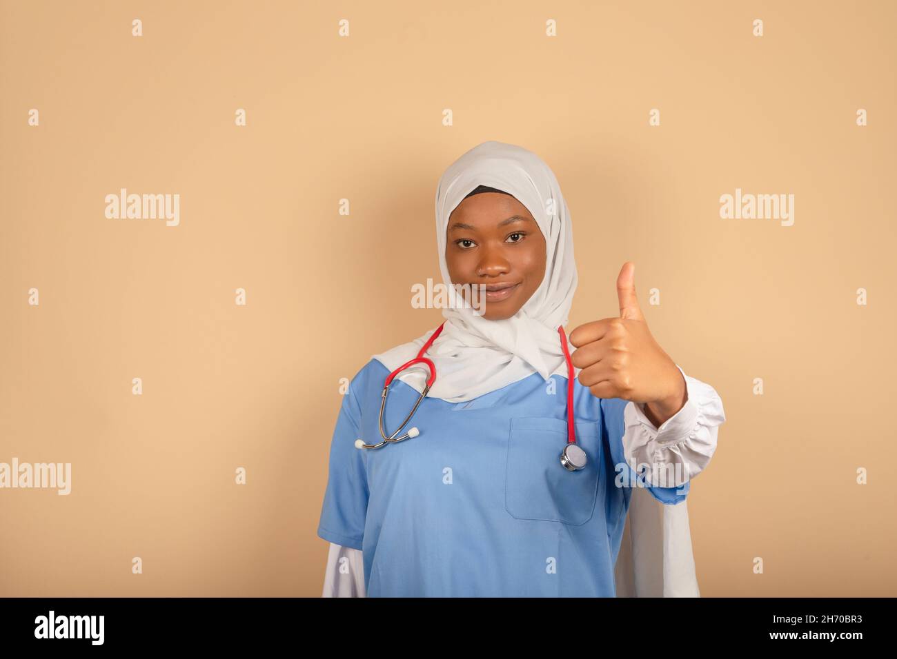 African American nurse with headscarf showing thumb up, posing on light background, free space Stock Photo