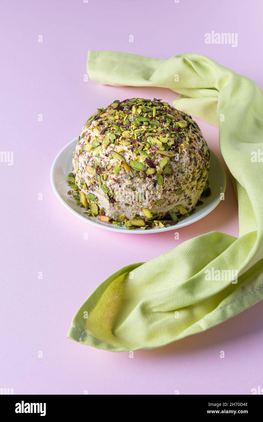 Sesame halva with pistachios on white plate on pink background with green linen napkin. High angle view. Traditional middle eastern sweets. Jewish, tu Stock Photo