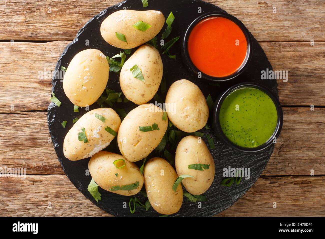 Canarian Wrinkly Potatoes Papas Arrugadas with a mojo rojo and mojo verde sauces close up in the plate on the table. Horizontal top view from above Stock Photo