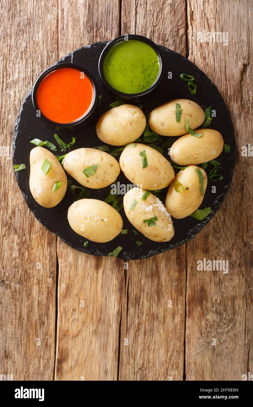Papas arrugadas wrinkly potatoes is a traditional boiled potato dish served with a mojo rojo and mojo verde sauces close up in the plate on the table. Stock Photo
