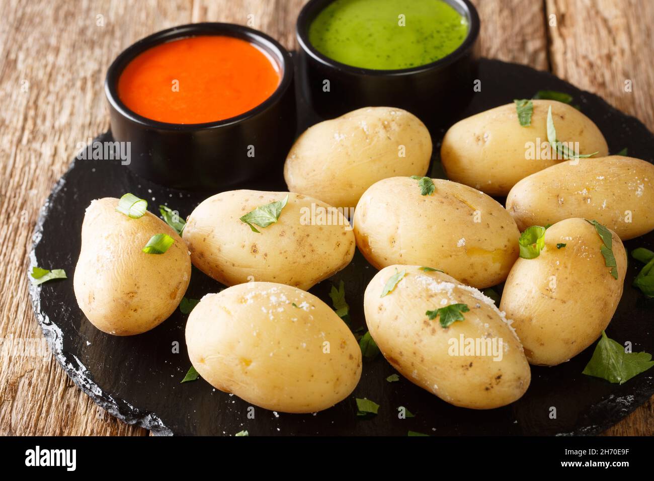 Canarian Wrinkly Potatoes Papas Arrugadas with a mojo rojo and mojo verde sauces close up in the plate on the table. Horizontal Stock Photo