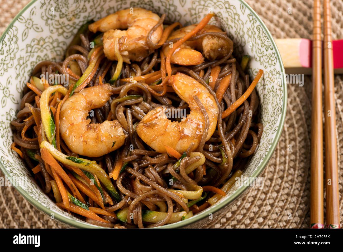 Ceramic bowl of delicious Yakisoba noodles wok with shrimps in brown sauce, served with chopsticks, viewed from above in close-up Stock Photo