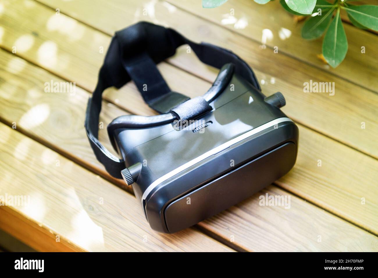 From above of modern black virtual reality glasses placed om wooden table near green potted plant on sunny day Stock Photo