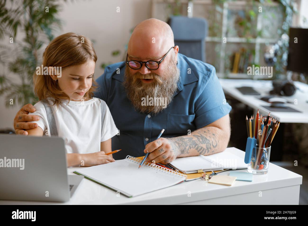 Careful daddy explains task to little daughter at table during video lesson in room Stock Photo