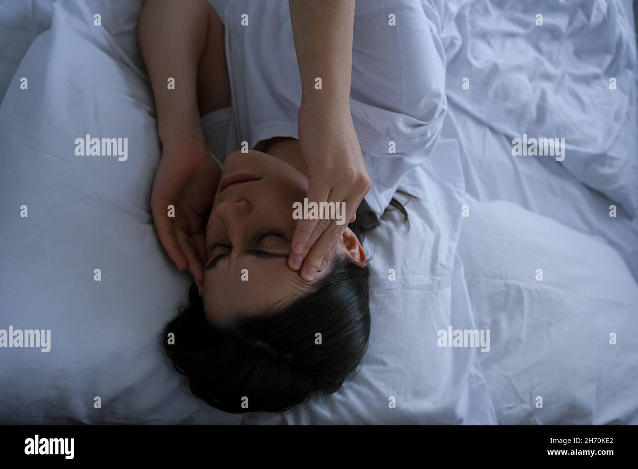Unhappy thoughtful young woman holding hands on forehead, feeling sad lonely lying in bed alone trying to sleep thinking of problem, fears Stock Photo