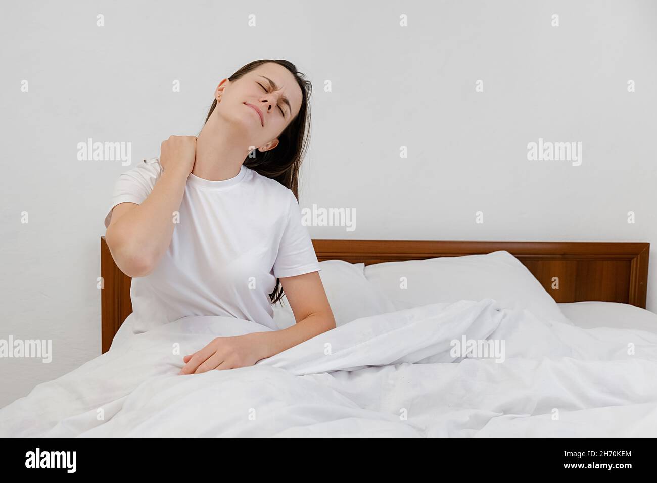 Fibromyalgia and backache concept. Unhappy young girl waking up in uncomfortable bed feeling ache in back pain massaging tensed muscles of stiff neck Stock Photo