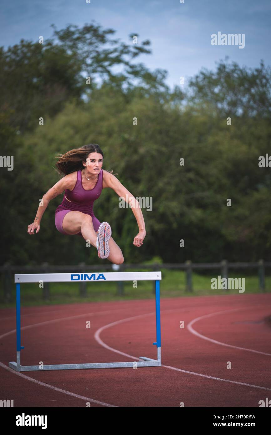 Athlete model girl jumping hurdles on the running track Stock Photo Alamy