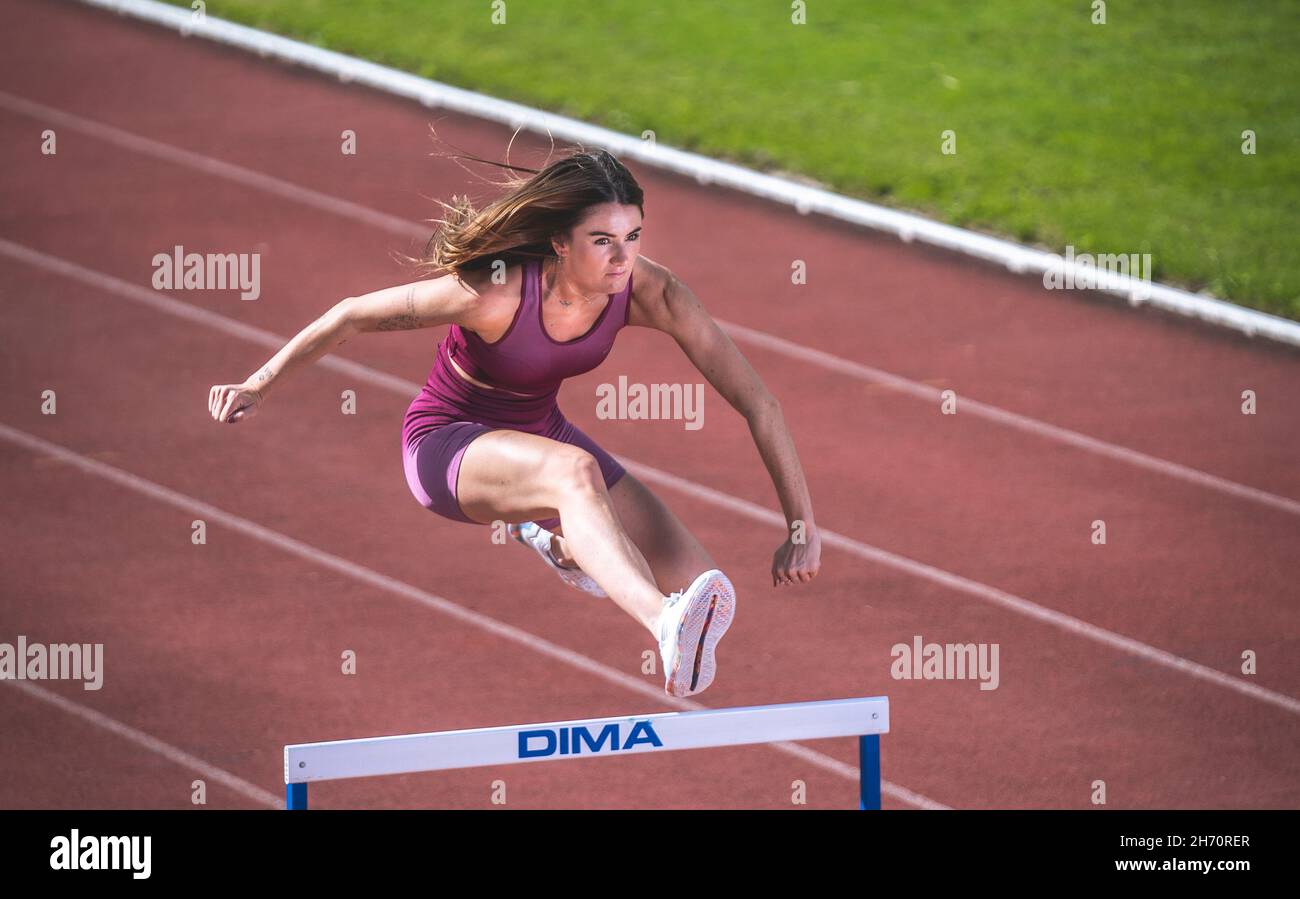 Athlete model girl jumping hurdles on the running track Stock Photo Alamy