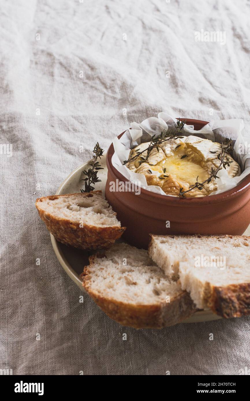 Small dish of baked camembert fondue topped with fresh thyme served in a small terracotta dish with bread. Stock Photo
