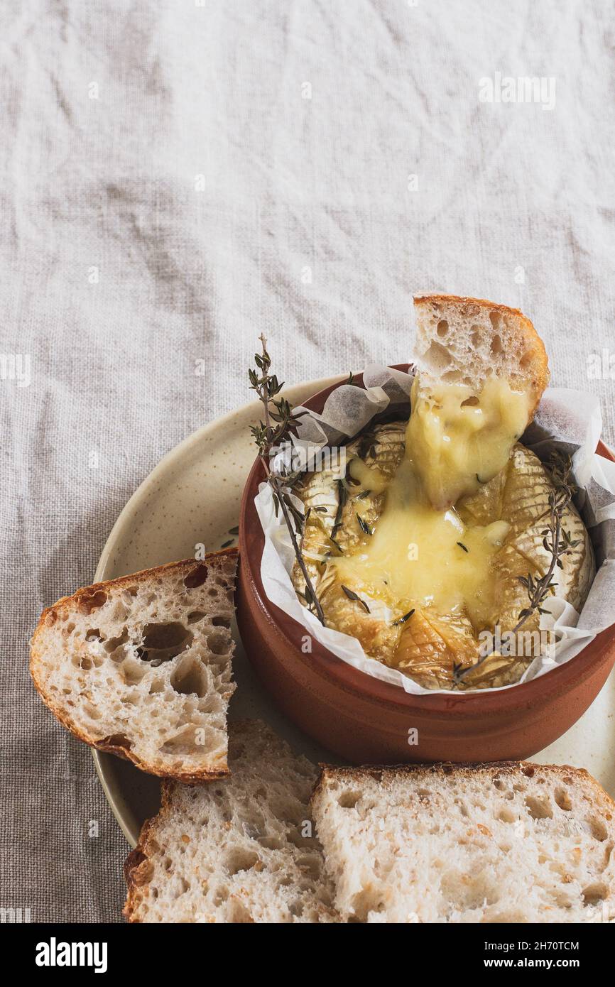 Piece of sourdough bread dipped in a dish of camembert cheese fondue. Stock Photo