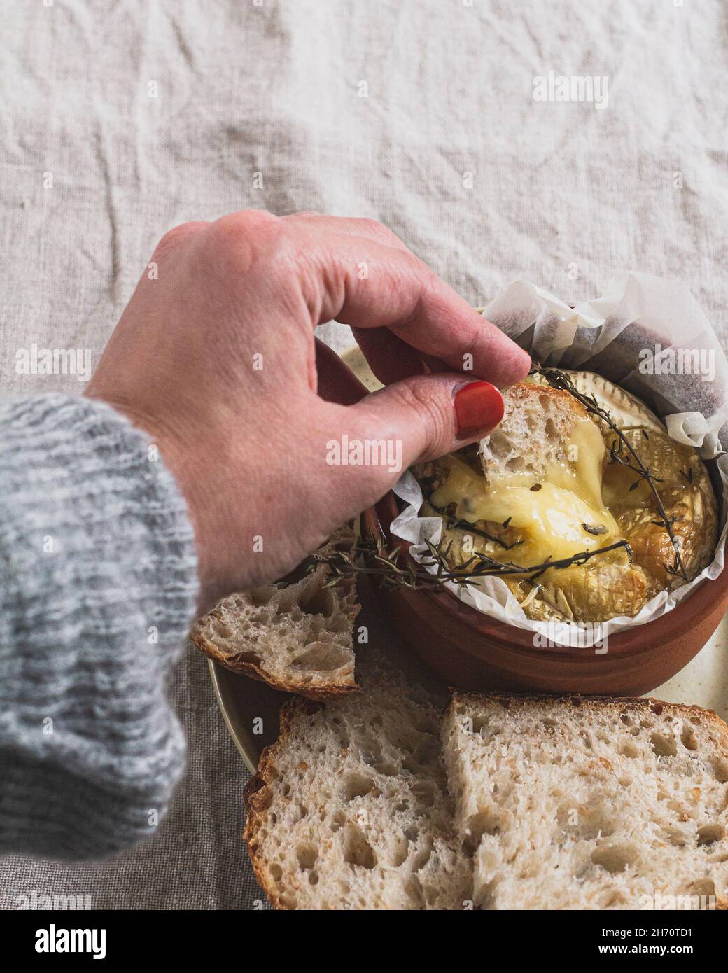 Hand dipping a piece of sourdough bread in a dish of camembert cheese fondue. Stock Photo