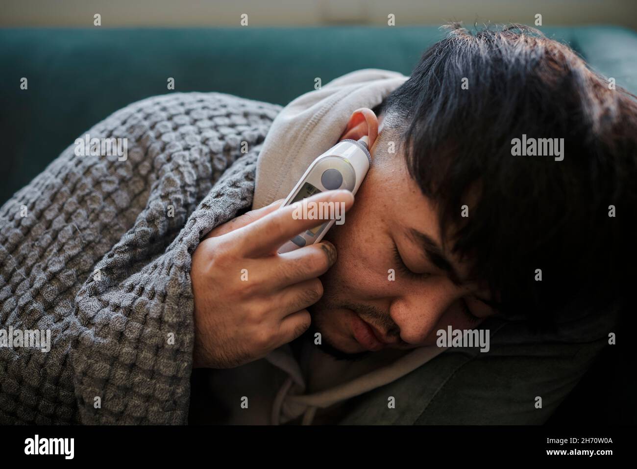 Ill man on sofa checking temperature Stock Photo