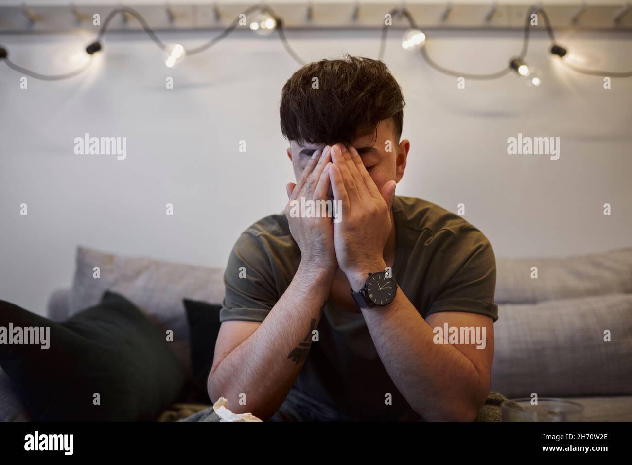 Ill man on sofa with face in hands Stock Photo
