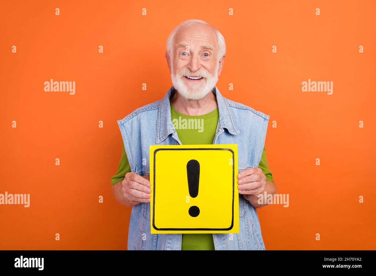 Photo of pretty handsome retired man wear vintage jeans waistcoat holding exclamation point sign smiling isolated orange color background Stock Photo