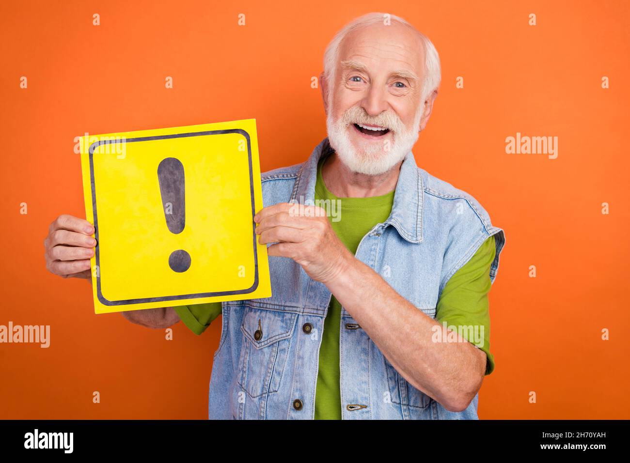 Photo of handsome cute retired man wear vintage jeans waistcoat holding exclamation point placard smiling isolated orange color background Stock Photo
