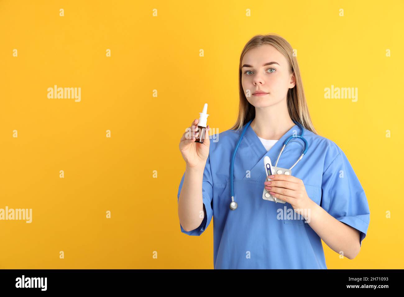 Young nurse with nasal spray on yellow background, seasonal cold