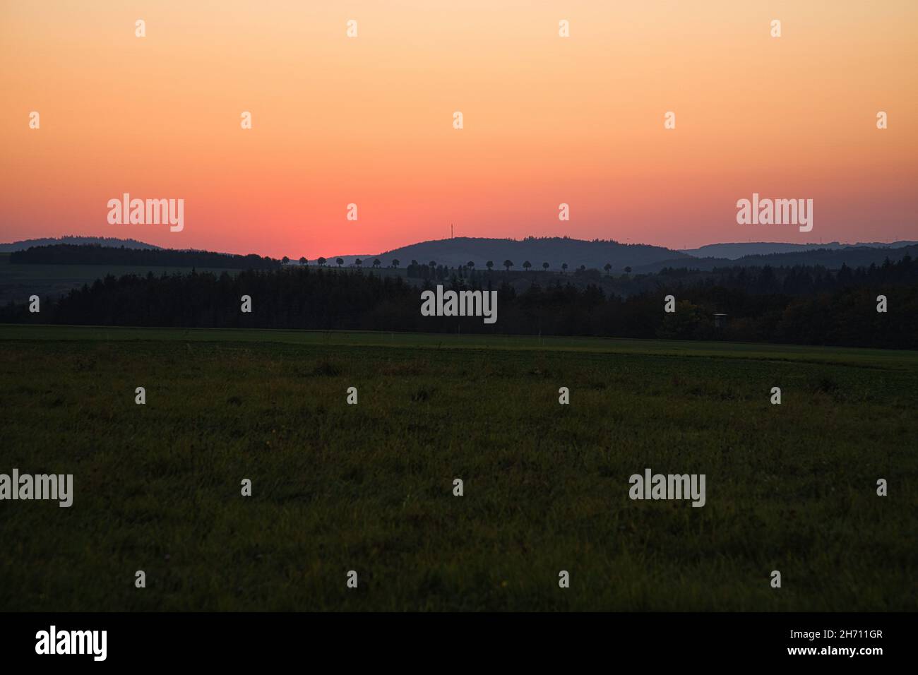 romantic sunset behind a hill in front of a meadow. Tuscan view with the row of trees in the background Stock Photo