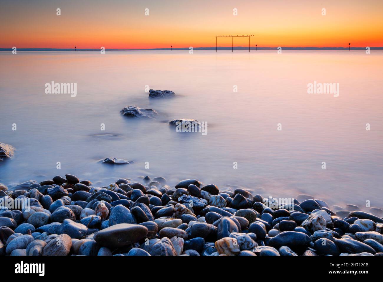 View from Arbon over Lake Constance at sunrise, with stones in the foreground and photographed with slow shutter speed, Switzerland Stock Photo