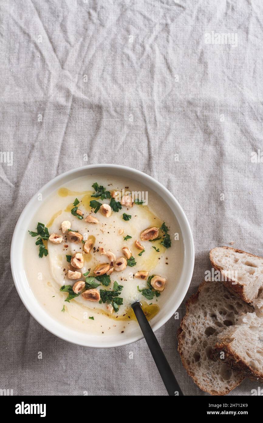 Bowl of celeriac soup topped with chopped parsley and hazelnuts, served with pieces of sourdough bread. Stock Photo