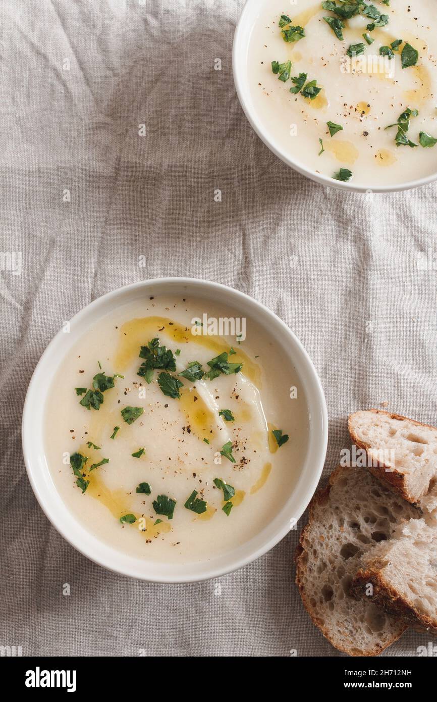 Two bowls of celeriac soup topped with olive oil and chopped parsley and served with pieces of sourdough bread. Stock Photo