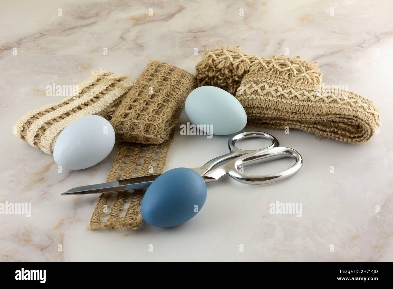 Blue Easter eggs, textured ribbons, and scissors on table for crafting project for Easter holiday Stock Photo