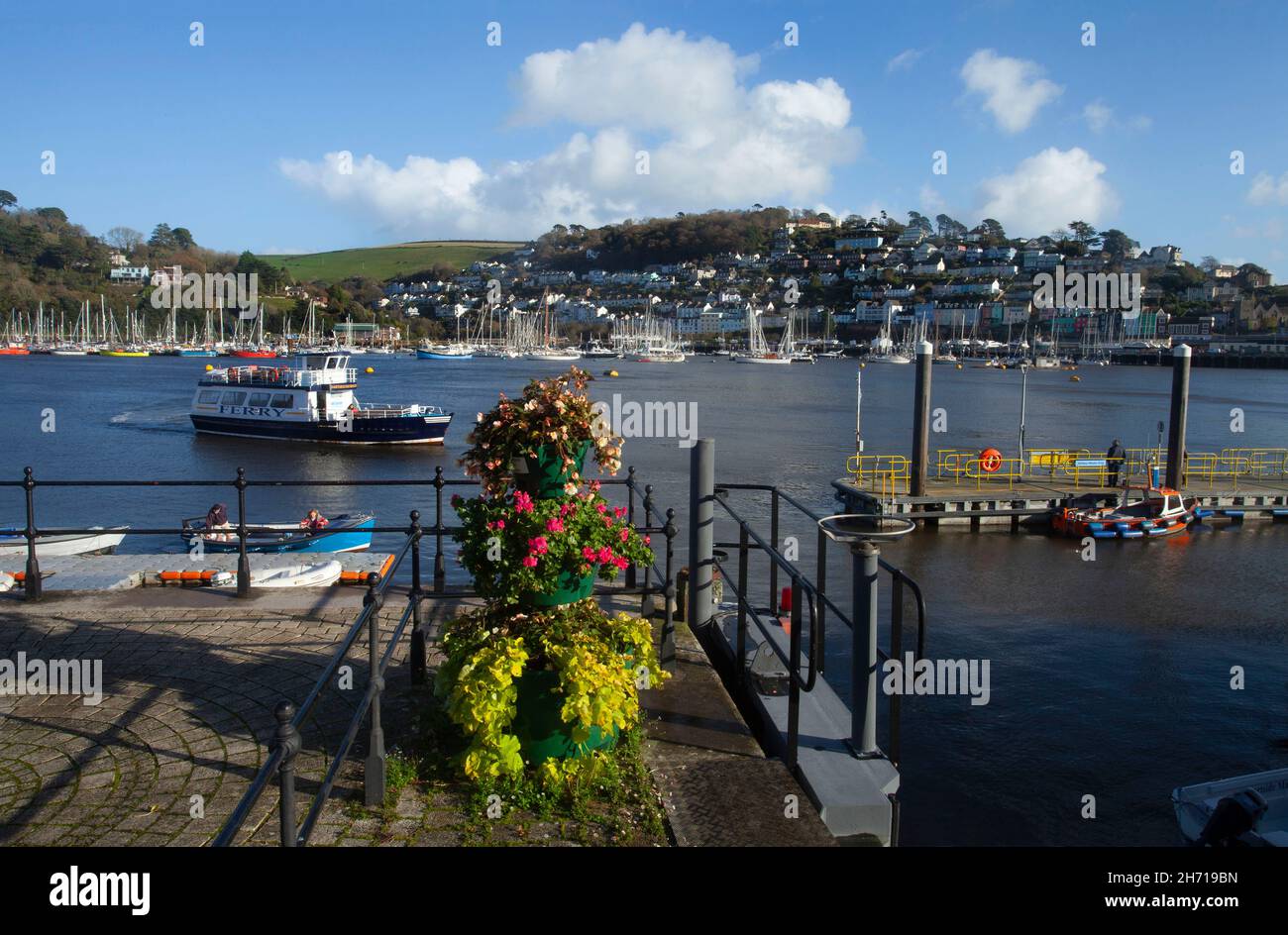 River Dart from Dartmouth side looking towards Kingswear Ferry on river yachts and flower arrangement on the quayside in summer blue sky copy space Stock Photo