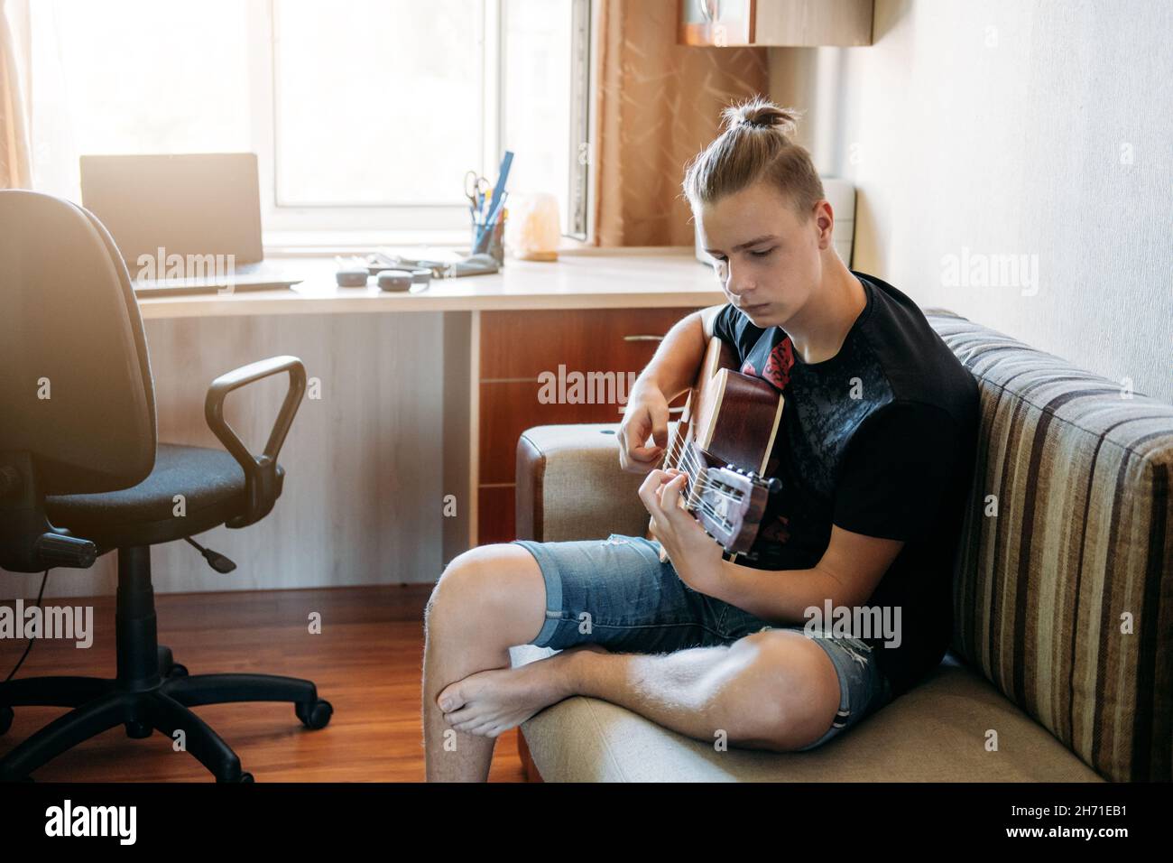 Guitar lessons for beginners. Caucasian teenager playing guitar, having Online Guitar Lessons, enjoying favorite hobby, leisure. Acoustic guitars for Stock Photo