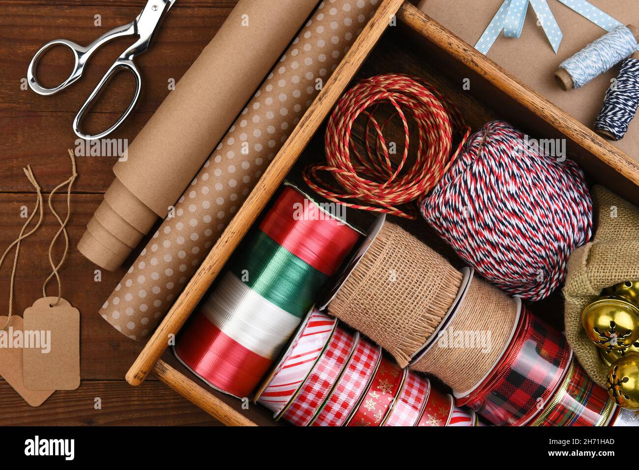 Christmas Flat Lay - Box of Christmas present wrapping supplies with wrapping paper and gift tags on a dark rustic wood table. Stock Photo