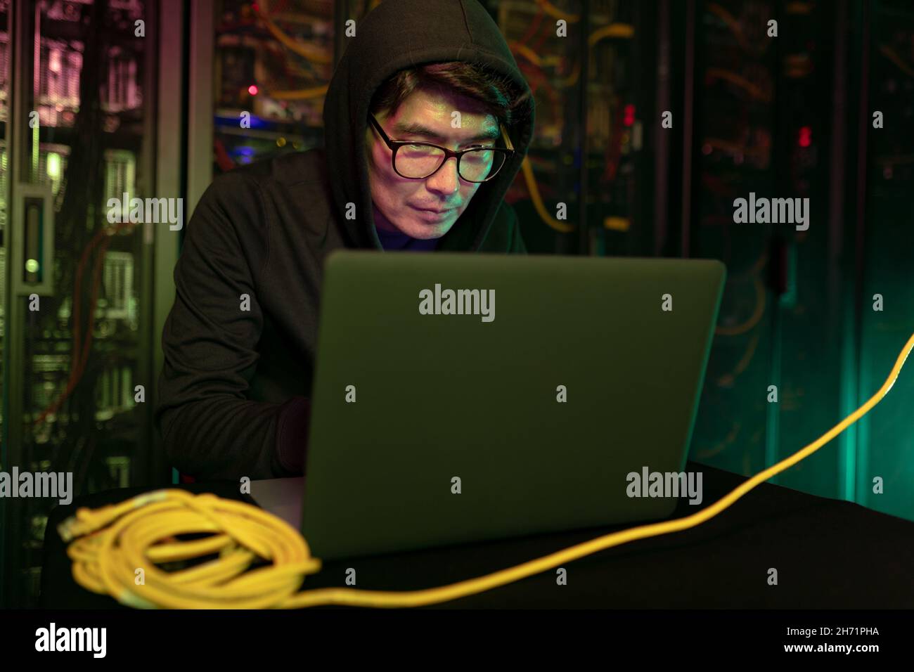 Asian male hacker using a laptop in computer server room Stock Photo