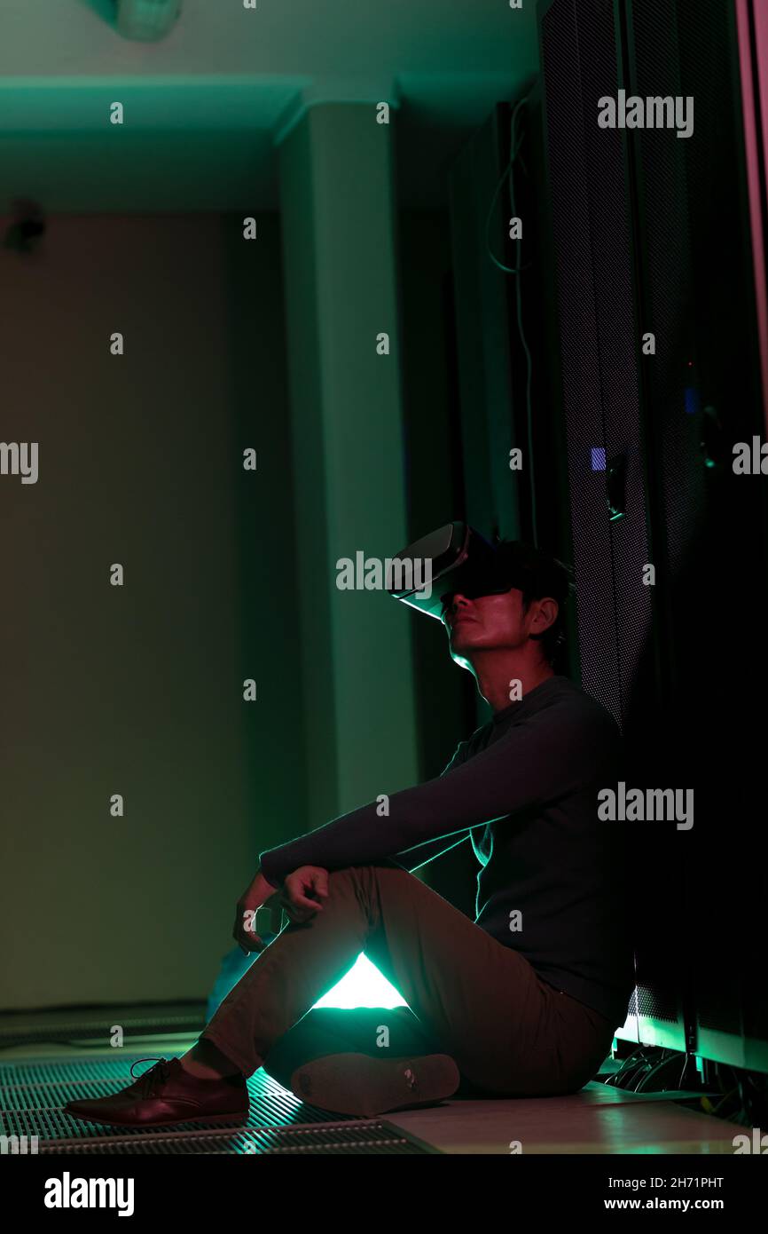 Asian man wearing vr headset while sitting in computer server room Stock Photo