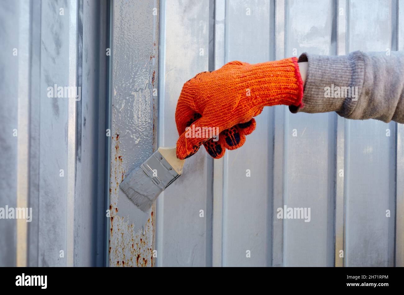 Painting the fence. Woman's hand painting steel fence with a brush Stock Photo