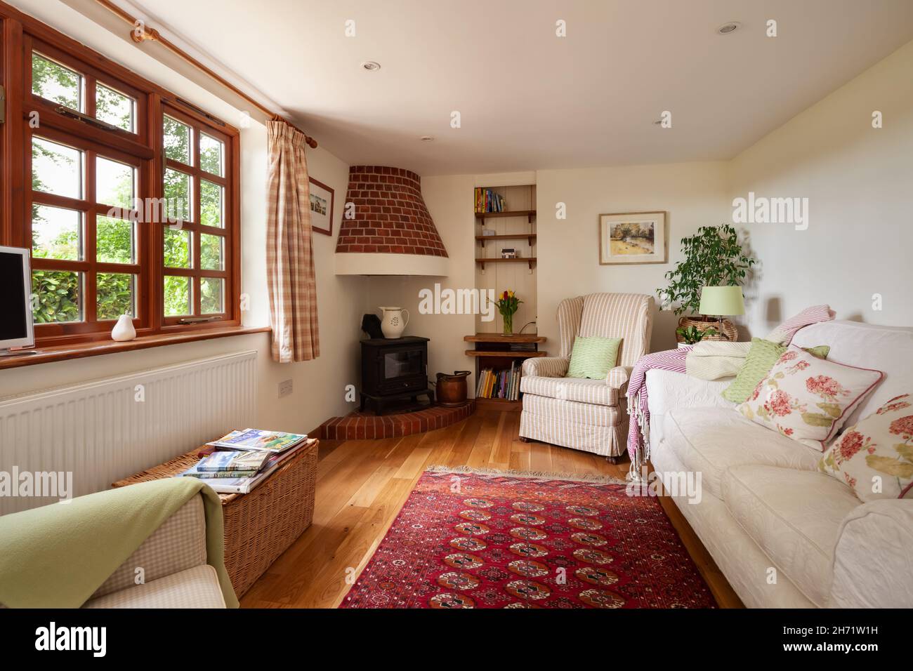 Whepstead, Suffolk, England - June 2 2020: Traditional home interior with exposed beams and brick fireplace with stove. Furnished with rug and sofa Stock Photo