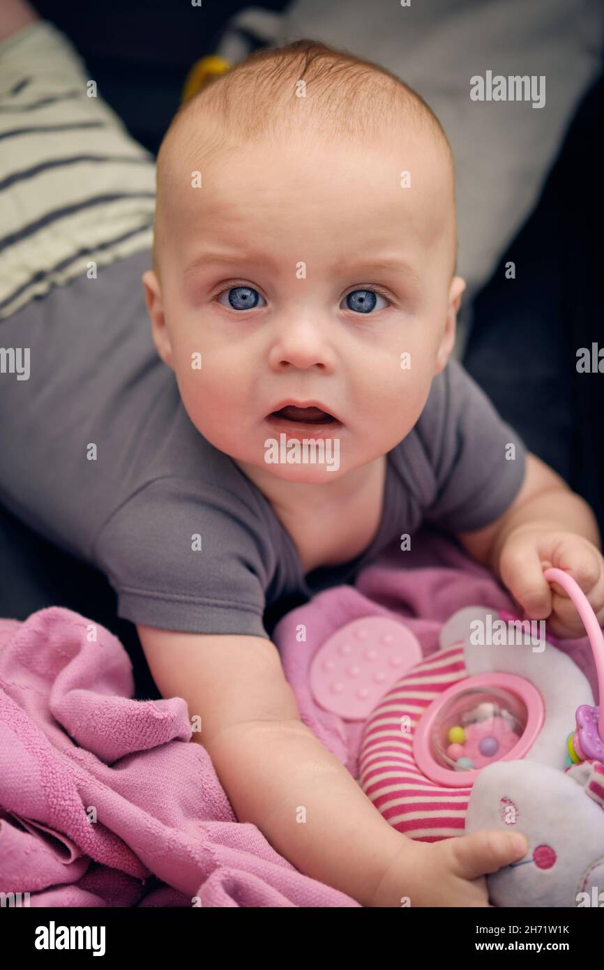 A cute baby is lying on a pink blanket and is looking at the camera Stock Photo