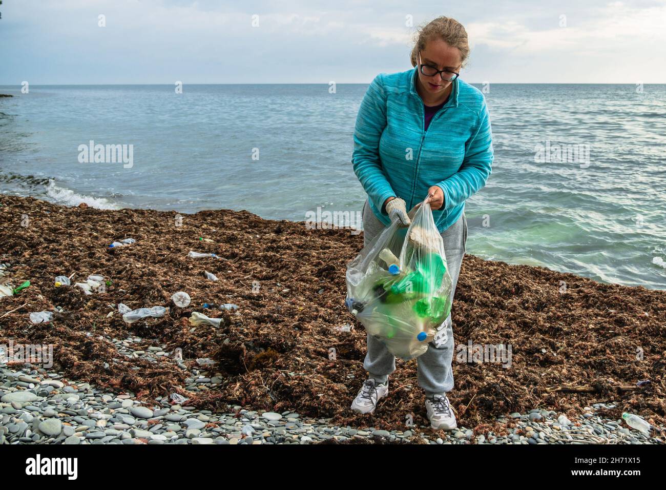 A Caucasian woman volunteers to clean the stone beach of plastic trash. An  eco-activist cleans the shore from pollution. The concept of caring for nat  Stock Photo - Alamy