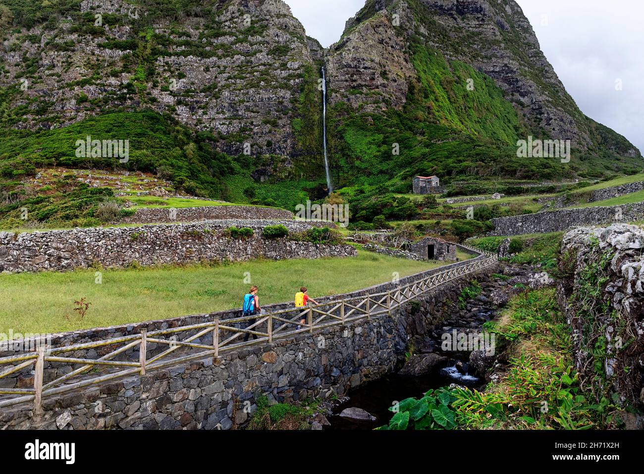Mother and son walking on stone path to the Cascata do Poco do Bacalhau waterfall, a rock Mother and son walking on stone path to the Cascata do Poco do Bacalhau waterfall, a rock
