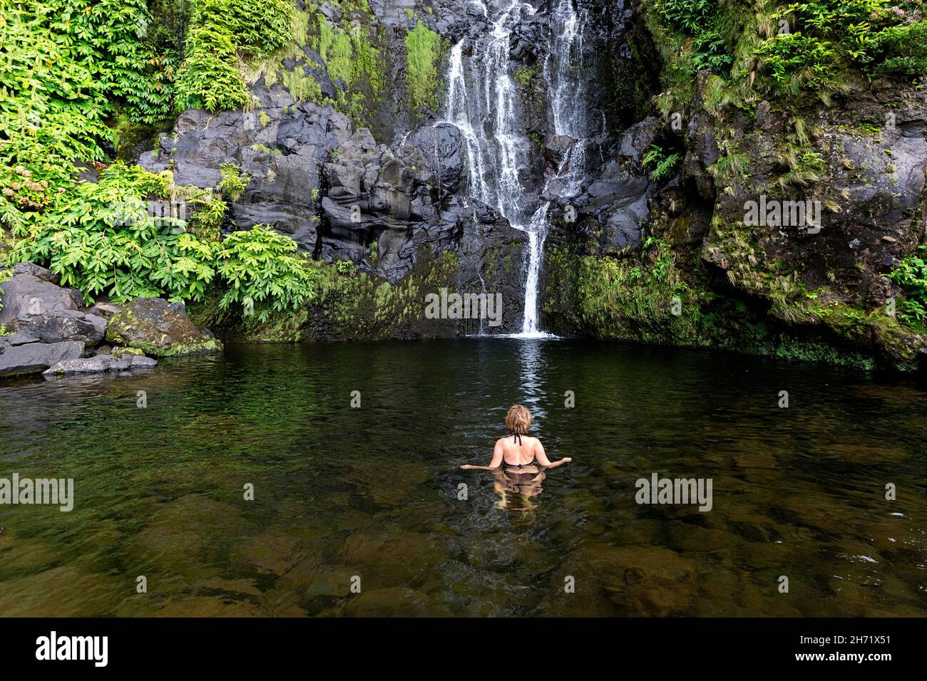 Woman bathing under waterfall shower in natural swimming pool at Cascata do Poco do Bacalhau Woman bathing under waterfall shower in natural swimming pool at Cascata do Poco do Bacalhau