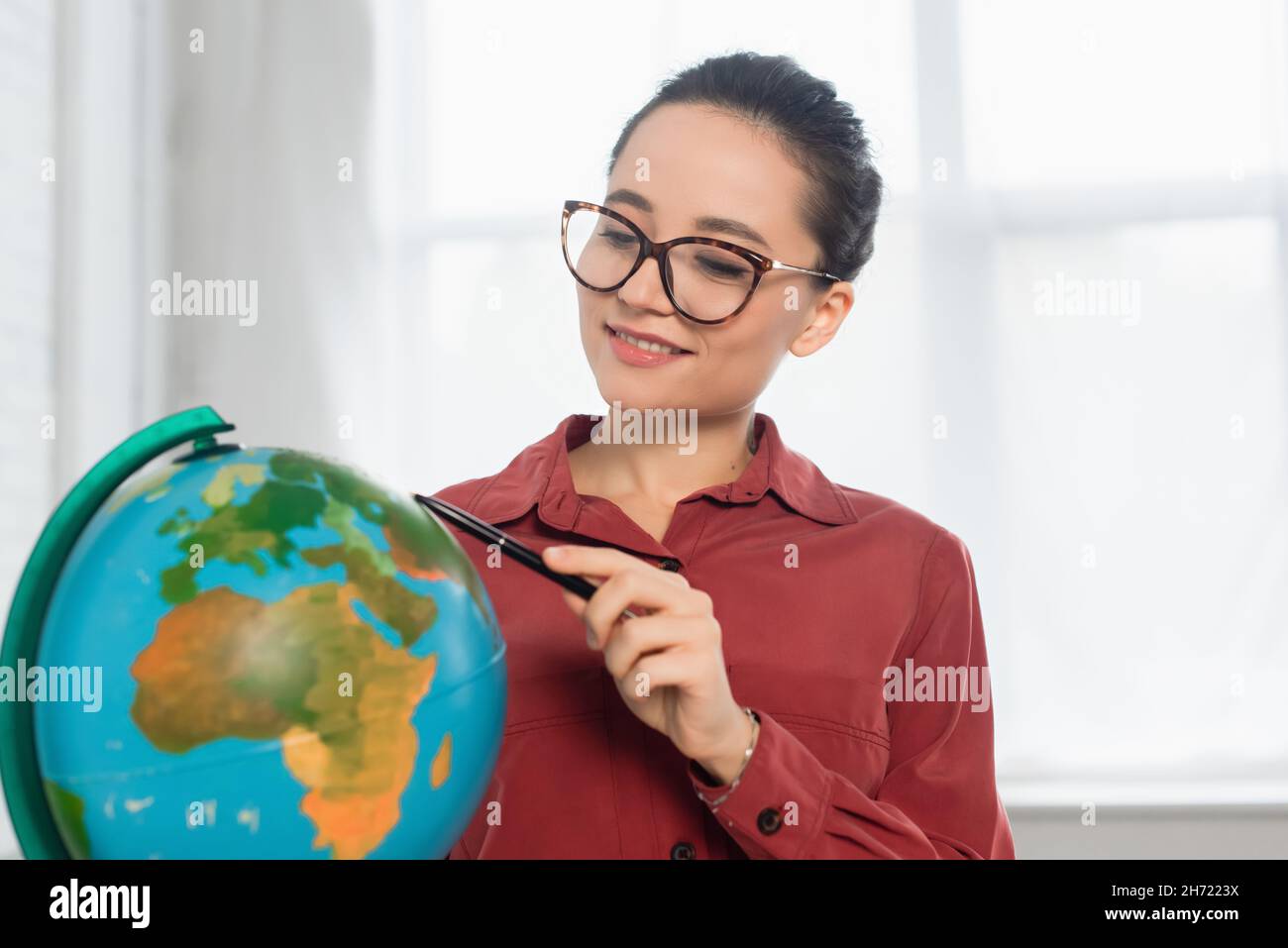 cheerful teacher in eyeglasses holding pen near globe Stock Photo - Alamy