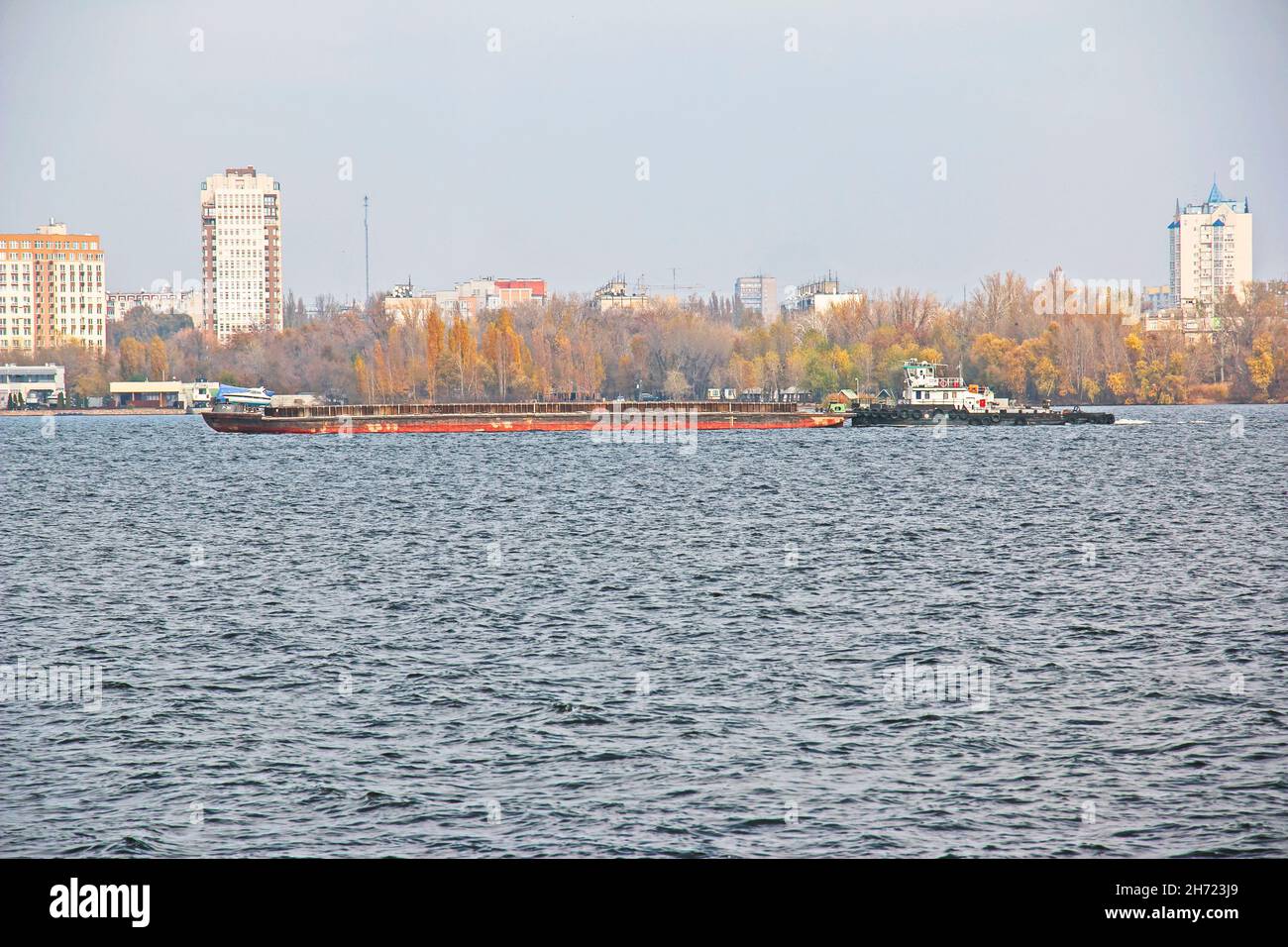 An articulated tug and bulk barge transport sand and construction materials along the river. A large barge sails along the wide Dnieper River. Transpo Stock Photo