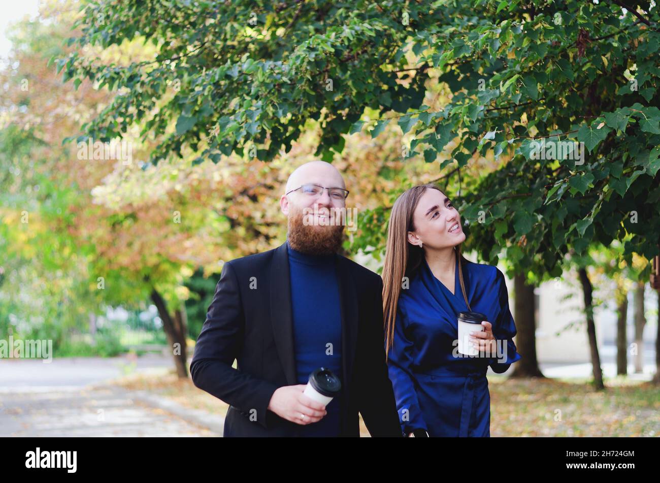 Happy family, couple drinking coffee in city. Urban love story of a stylish young business man in a blue suit with a red beard. And attractive woman Stock Photo